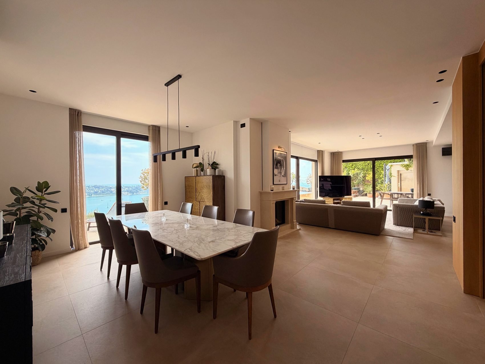 Dining table beside floor-to-ceiling windows framing the bay of Villefranche